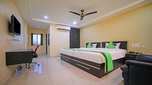 A hotel room with a bed, a desk, a chair, a television, and a ceiling fan. - Staro Hotel - Hotel In Vijayawada (Vijayawada)