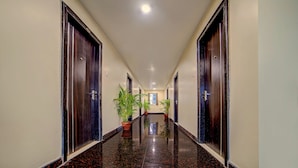 A long, polished hallway with dark wooden doors on both sides, leading to a room with a window and a potted plant. - Staro Hotel - Hotel In Vijayawada (Vijayawada)