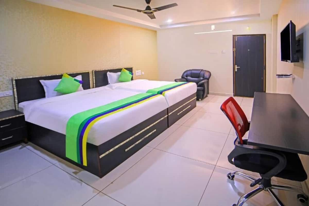Une chambre d’hôtel avec deux lits, un bureau, une chaise, une télévision et une porte.