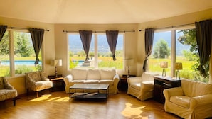 Ein geräumiges Wohnzimmer mit Holzboden, einer Sofagarnitur und einem Couchtisch. Große Fenster bieten Blick auf einen Pool und Grünflächen.