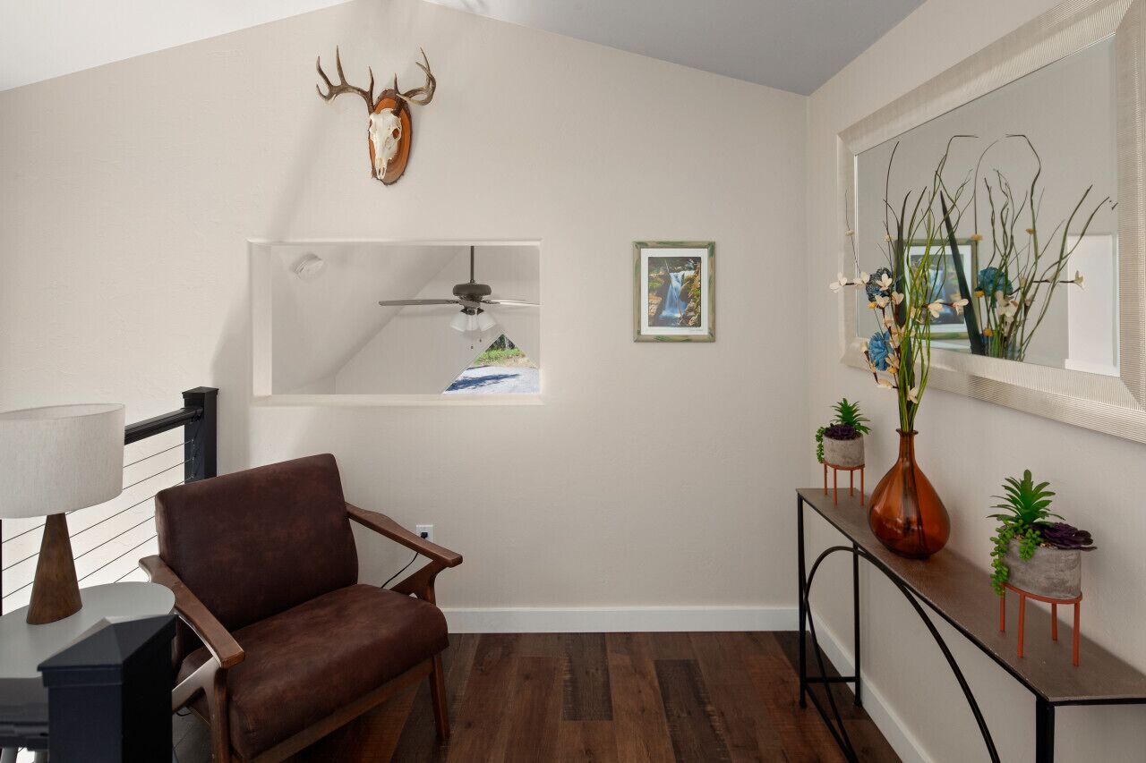 A modern living room with a brown leather chair, a ceiling fan, a mounted deer skull, a framed picture, and a console table with potted plants.