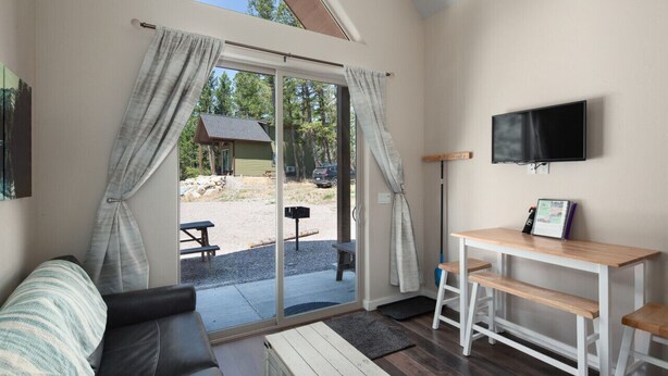 Una habitación acogedora con una puerta corredera de cristal que da a un espacio al aire libre, un televisor de pantalla plana montado en la pared y una pequeña mesa de madera con bancos.
