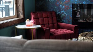 Una habitación con un sillón tapizado de terciopelo rojo, una mesita redonda con una bebida y una pared con estampado.
