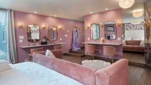 Ein Hotelzimmer mit einem großen Bett, einem Schminktisch mit Spiegeln, einer Sitzecke mit Stühlen und einem kleinen Schreibtisch.