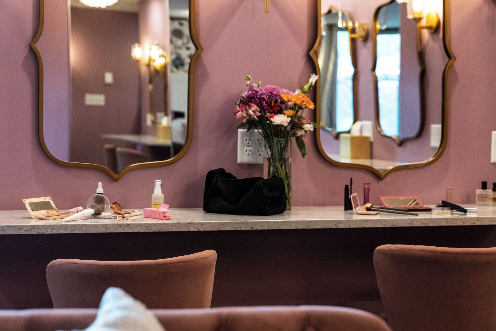 A salon with a vanity counter, mirrors, and a vase of flowers.