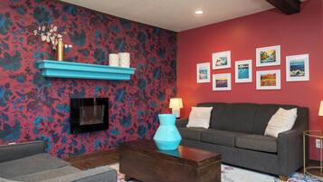 A living room with a fireplace, a sofa, a coffee table, and a wall with framed pictures.