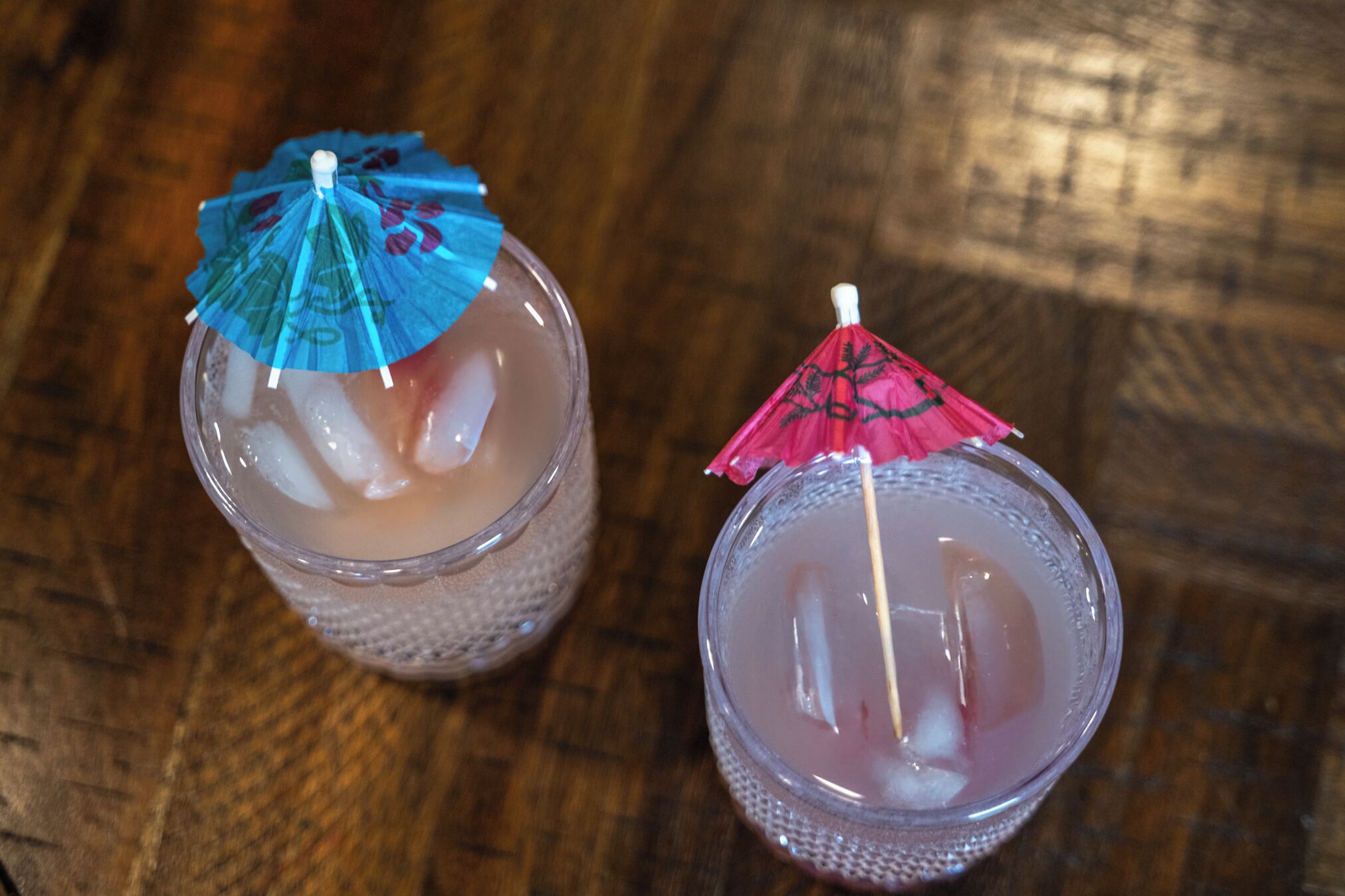 Two glasses of iced drinks with umbrellas on a wooden surface.