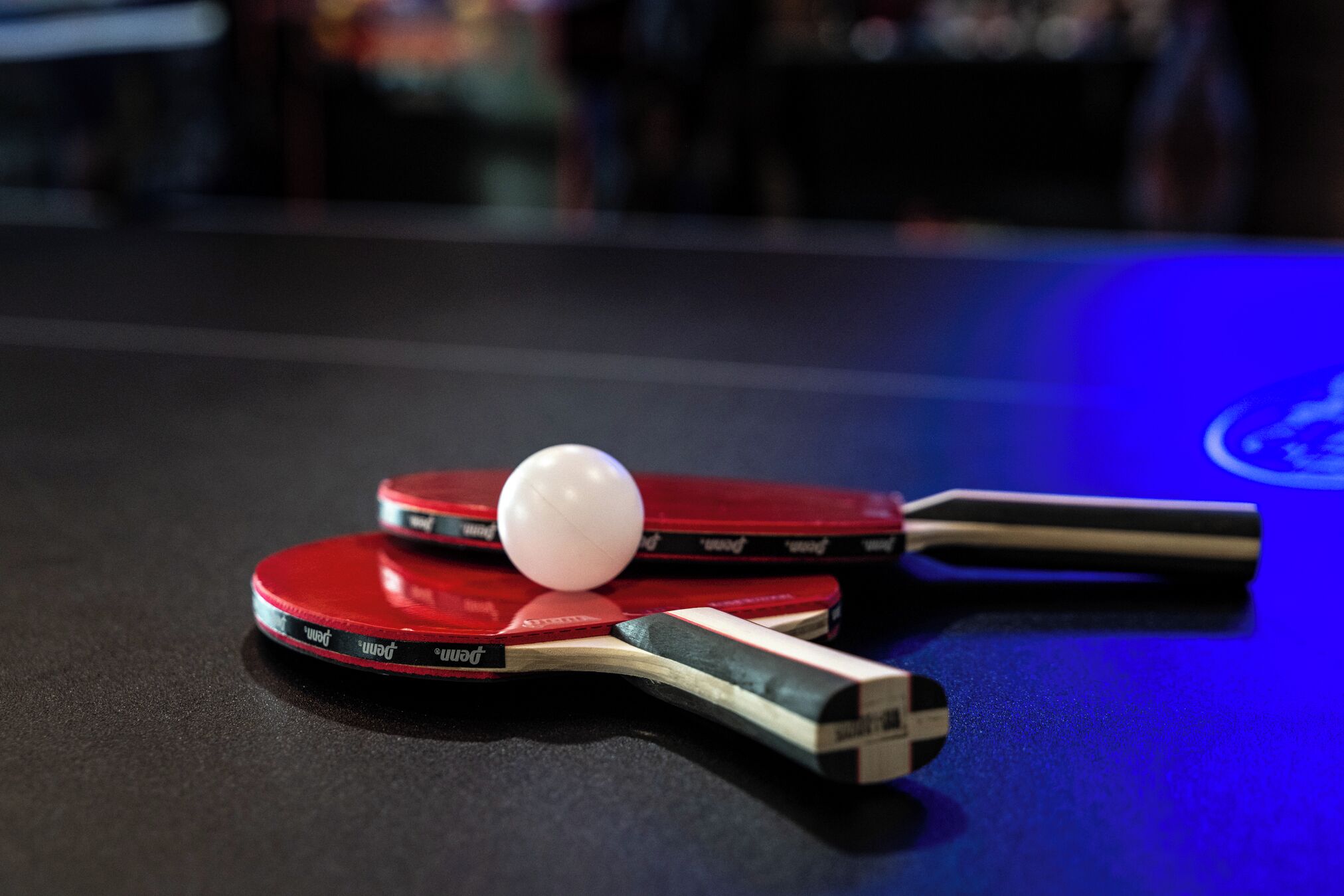 Una mesa de ping pong con dos paletas rojas y una pelota blanca.