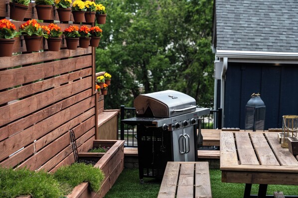 A backyard with a wooden fence, a barbecue grill, and a wooden table.