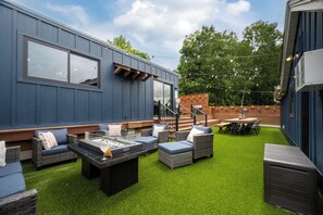 A modern outdoor patio with artificial grass, wicker furniture, and a barbecue area.