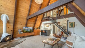 Ein geräumiger Loft mit hoher Decke, freiliegenden Holzbalken, Kamin, Küchenzeile und einer Wendeltreppe zu einer oberen Ebene.