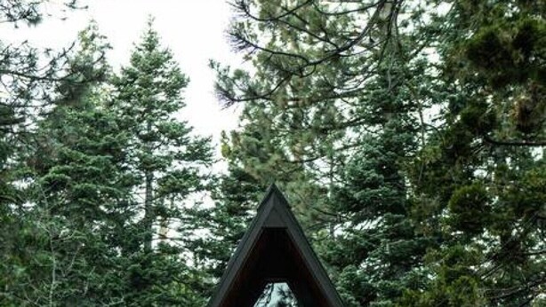 Eine Hütte mit einem Giebeldach, großen Fenstern und einer Veranda mit Lichterketten.