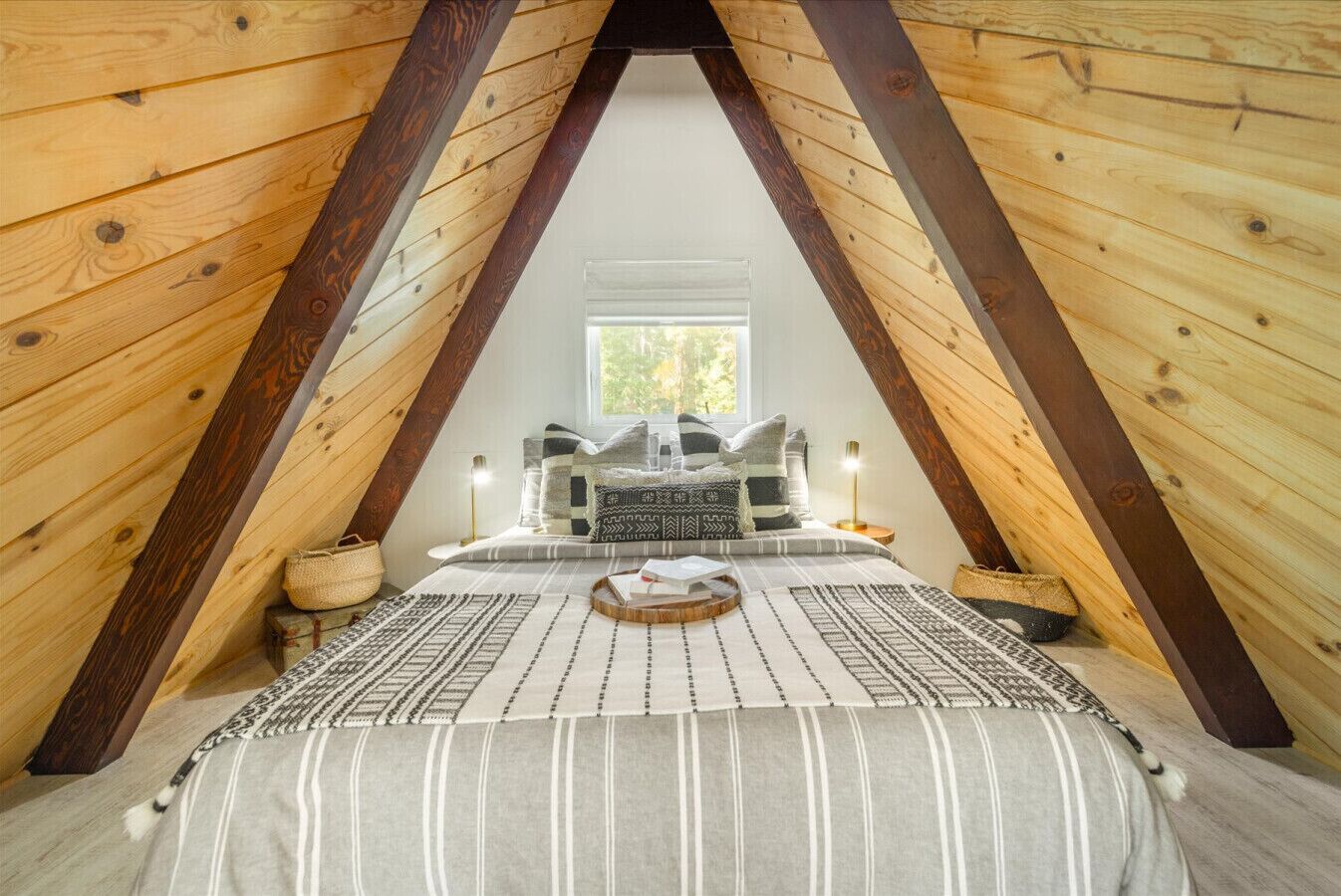 A cozy attic bedroom with a sloped ceiling, a bed with patterned bedding, and a window providing natural light.