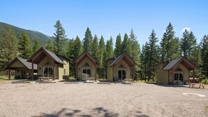 Tres cabañas de madera en fila, cada una con amplias ventanas y una mesa de picnic al frente.