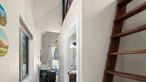 Un pasillo estrecho con una escalera de madera, una ventana con vistas y una puerta que da a un baño.