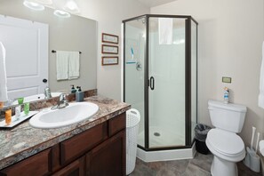 A bathroom with a granite countertop sink, a glass shower enclosure, and a white toilet. - Swift Current at 406 Glacier Cabins (Columbia Falls)