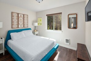 A bedroom with a bed, a nightstand, a lamp, a window, and a mirror. - Swift Current at 406 Glacier Cabins (Columbia Falls)