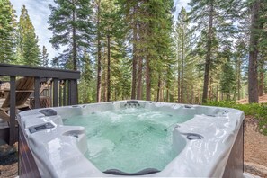 A hot tub in a forested area with a wooden deck and a covered seating area. - Northstar A-Frame Cabin with Hot Tub | Resort Shuttle, Sleeps 8 (Truckee)