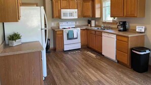 A compact kitchen with wooden cabinets, a microwave, a stove, a sink, and a coffee maker. - Sweet Escape, next to C-I bike/snowmobile trail. (Crosby)