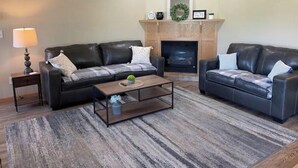 A living room with two black leather sofas, a wooden coffee table, a fireplace, and a rug. - Sweet Escape, next to C-I bike/snowmobile trail. (Crosby)