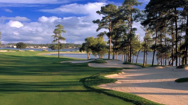 Ein Golfplatz mit Sandbunkern, Wasserhindernissen und einem Hintergrund aus Bäumen und einem See.