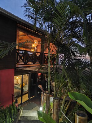 A two-story building with a balcony, large windows, and a well-lit interior. - nugget! Ocean view studio with private Jacuzzi in an exceptional tropical garden  (Les Avirons)