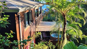 Ein Holzhaus mit Balkon, umgeben von üppigem Grün und Palmen.