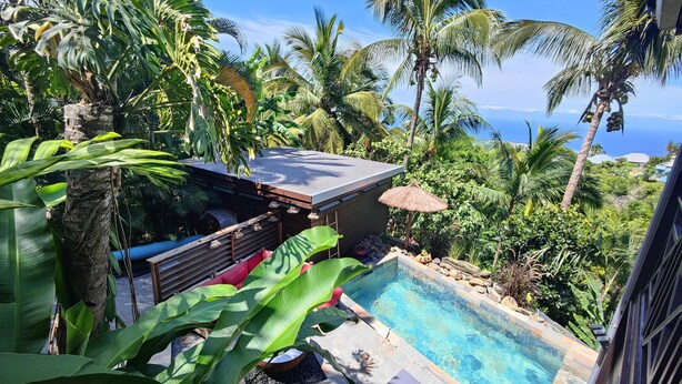 Ein Poolbereich mit Holzterrasse, Liegestühlen und einem Reetdachschirm.