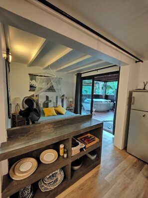 A modern kitchen with a dark wooden countertop, built-in shelves with plates, and a large window offering a view of the outdoors. - nugget! Ocean view studio with private Jacuzzi in an exceptional tropical garden  (Les Avirons)
