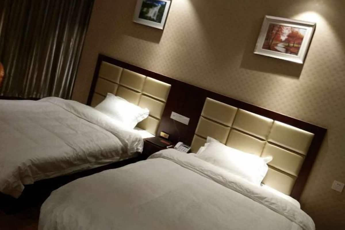Een hotelkamer met twee bedden, een hoofdbord, een nachtkastje en een aan de muur bevestigd telefoontoestel.