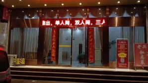 L’entrée d’un hôtel, avec une enseigne rouge indiquant les différents types de chambres et une affiche promotionnelle sur la droite.