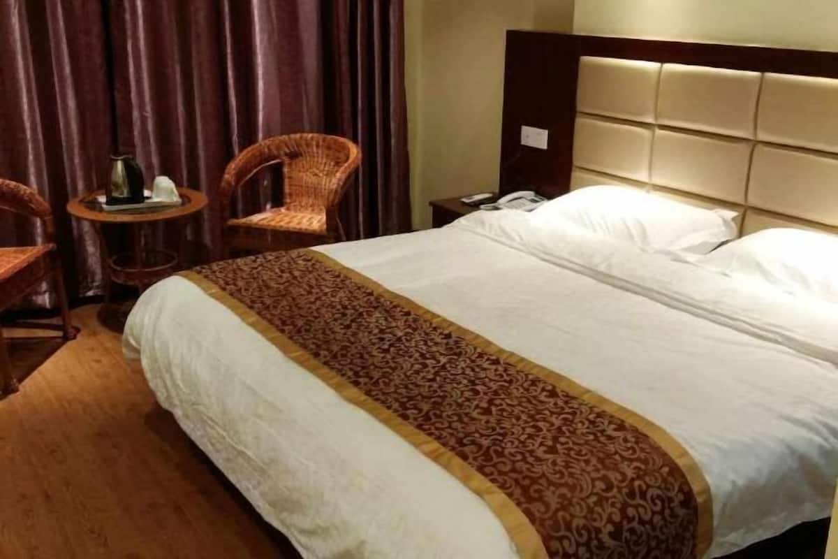 Een hotelkamer met een groot bed, een hoofdbord, een klein tafeltje met een lamp en twee rieten stoelen.