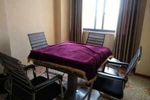 Un coin repas comprenant une table et quatre chaises, une nappe violette et une fenêtre avec des rideaux.