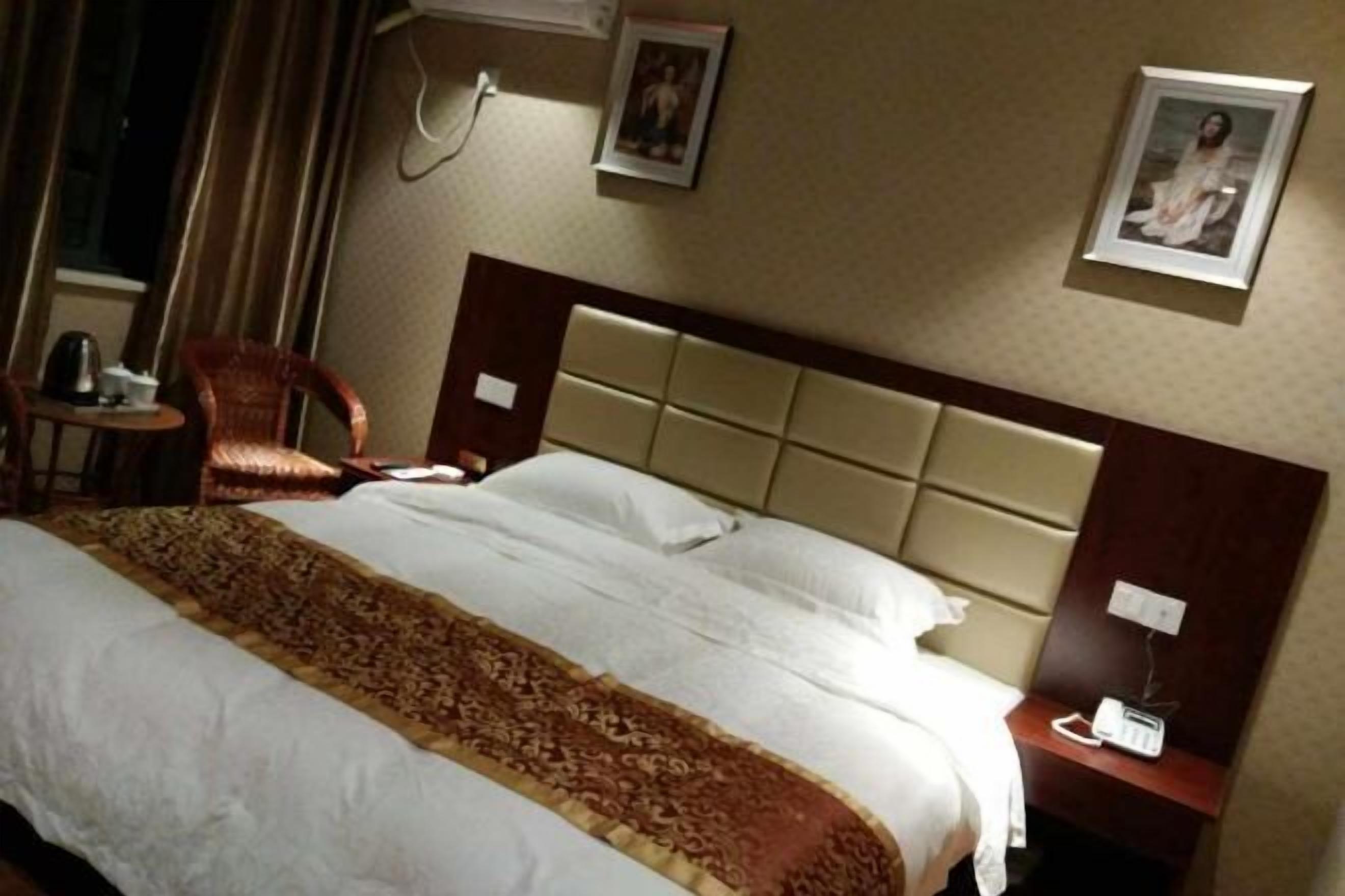 A hotel room with a bed, a chair, a bedside table, and a wall-mounted phone.