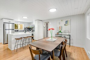 Una cocina moderna con armarios blancos, un refrigerador de acero inoxidable y una mesa de comedor de madera con taburetes de bar.