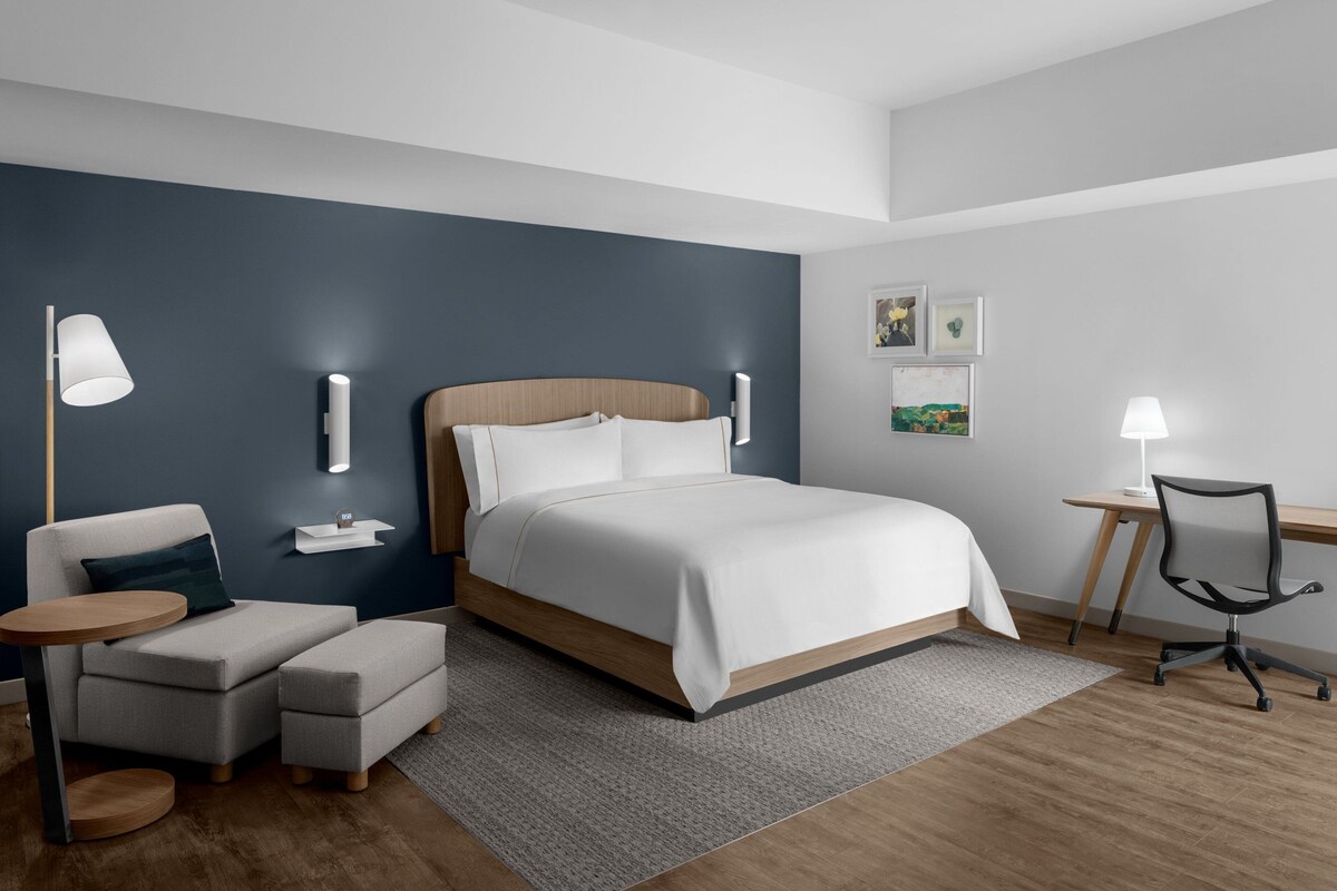Ein modernes Hotelzimmer mit einem großen Bett, einem Schreibtisch, einem Sessel und einer kleinen Couch.