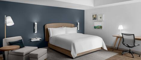 A modern hotel room with a large bed, a desk, a chair, and a small sofa.