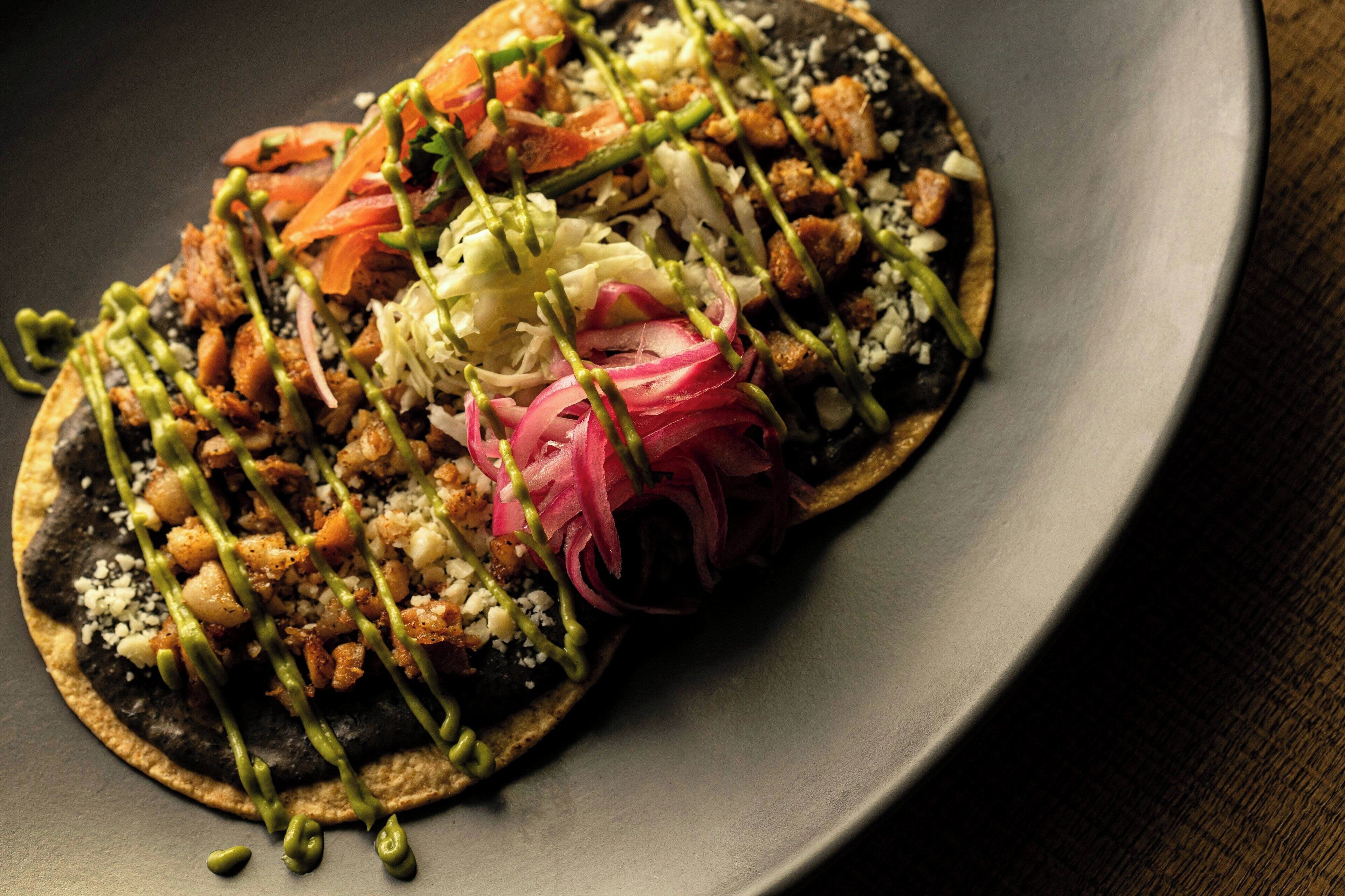Une assiette contenant une tortilla noire, recouverte de divers ingrédients et d’une sauce verte.