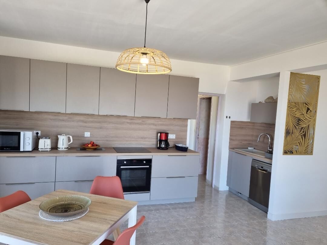 Une cuisine moderne avec des meubles gris, un plan de travail en bois, un luminaire suspendu et un coin repas comprenant une table et des chaises.