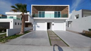 Una casa moderna de dos pisos con garaje, una palmera y cielo despejado.