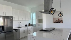 Una cocina moderna con armarios blancos, un refrigerador de acero inoxidable, una isla de mármol e iluminación colgante.