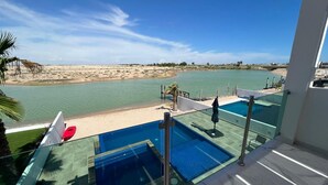 Un balcón con barandilla de vidrio que da a una piscina y una playa.