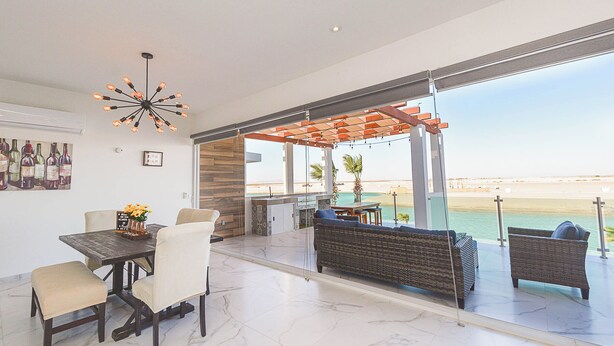 Una sala de estar moderna con comedor, ventanas amplias y vista al mar.