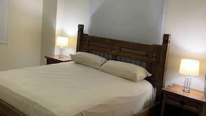 A standard hotel room with a wooden bed, two bedside tables with lamps, a plain wall, and a ceiling light. - Apartamento en el centro de la ciudad (La Romana)