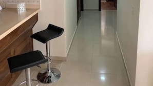 A narrow hallway with a kitchen area on the left, featuring wooden cabinets and a bar stool. - Apartamento en el centro de la ciudad (La Romana)