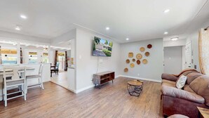 A spacious living room with a brown leather sofa, a dining area with white chairs, and a TV mounted on the wall. - Comfortable Family Home in Beautiful Neighborhood (Denver)