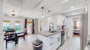 A modern kitchen with white cabinets, a granite countertop, and a built-in oven. There is a dining table with chairs and a trash can. - Comfortable Family Home in Beautiful Neighborhood (Denver)