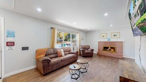 A modern living room with a brown leather sofa, a small round coffee table, a fireplace, and a large window with curtains. - Comfortable Family Home in Beautiful Neighborhood (Denver)