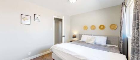 A bedroom with a bed, a nightstand, a wall-mounted lamp, and a door.