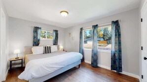 A bedroom with a bed, a nightstand, a window with curtains, and a view of the outside. - Comfortable Family Home in Beautiful Neighborhood (Denver)